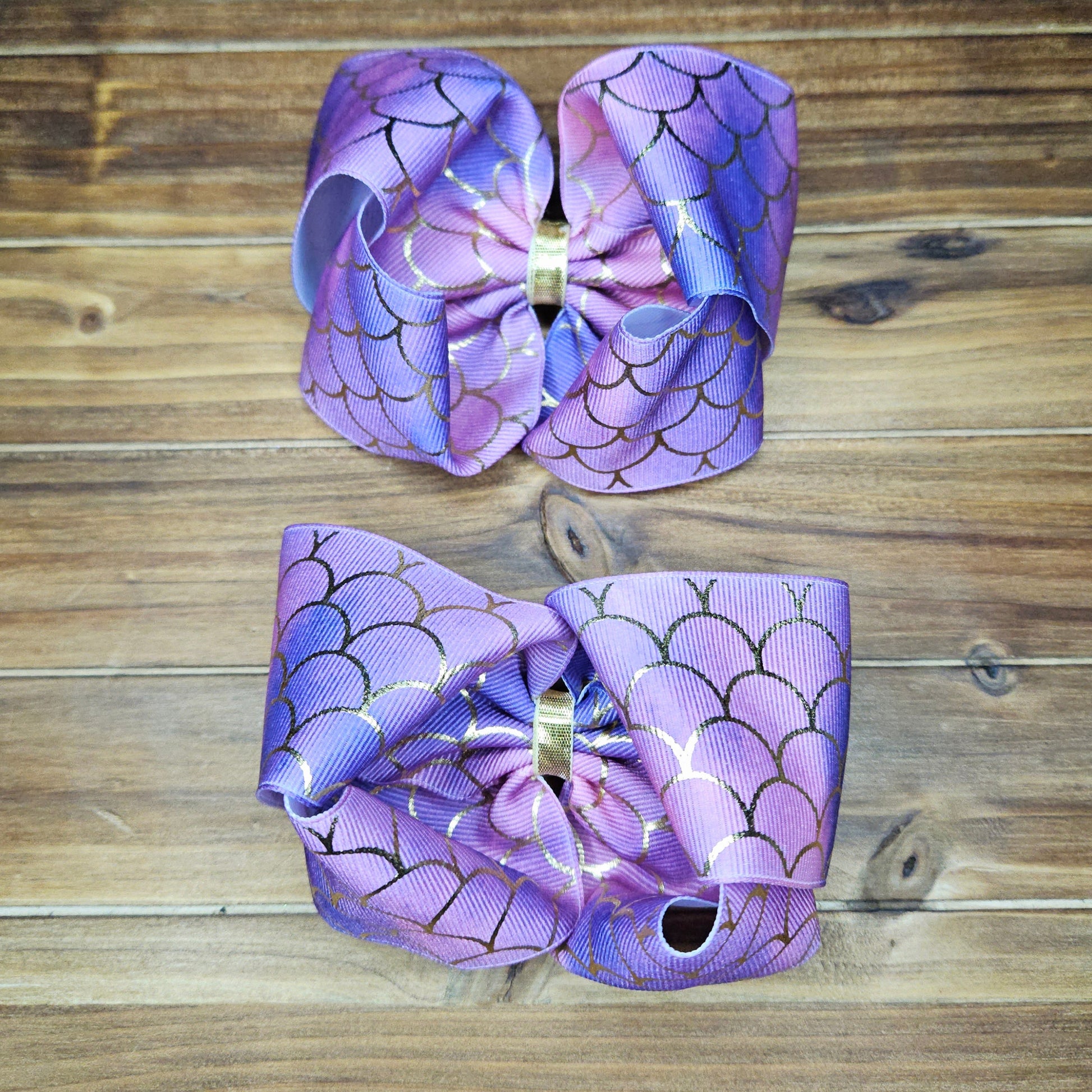 Two purple hair bows with gold centers on a wooden background